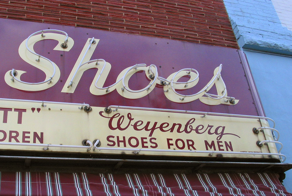 Photo of a hand-lettered metal/neon sign that says 'Shoes'