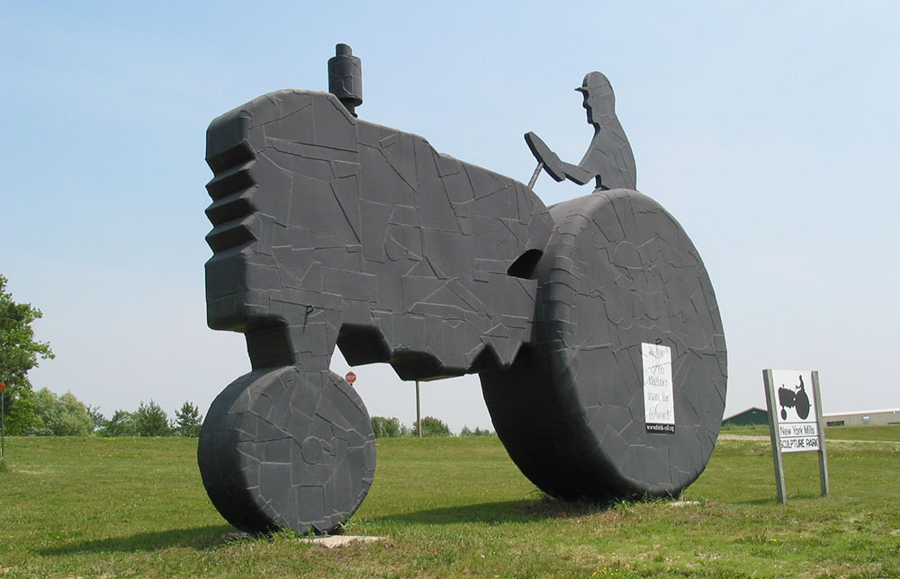 Photo of a large outdoor metal sculpture in the shape of a silhouette of a farmer on a tractor