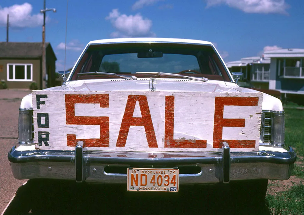 Photo of a large amateur-made ‘for sale’ sign on the front bumper of a car