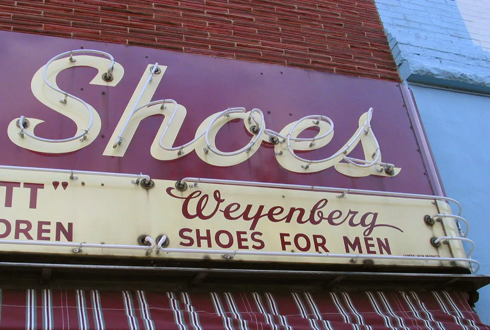 Photo of a hand-lettered metal/neon sign that says ‘Shoes’