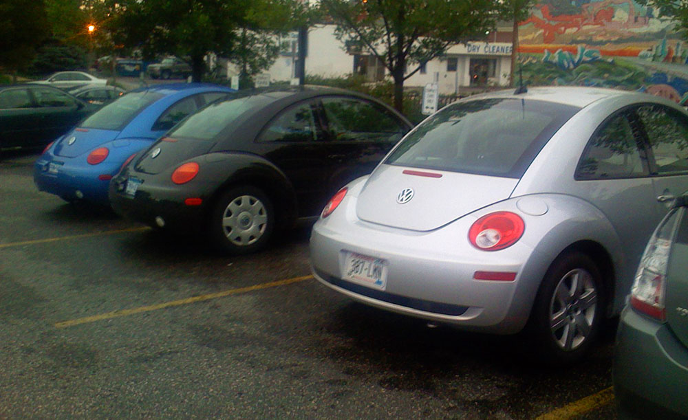 Blue, black and gray VW bugs in adjacent parking lot spaces.